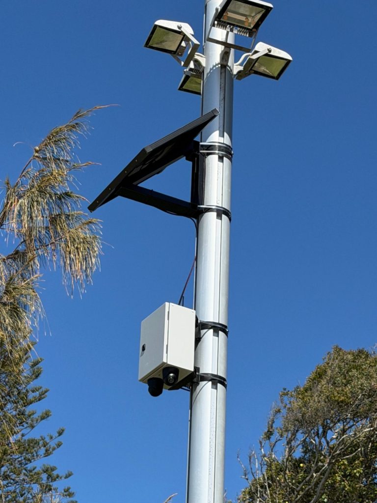 Solar CCTV camera box and solar panel mounted on a council floodlight pole using custom-fabricated brackets